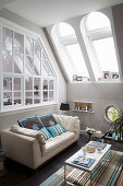 weiße Ledercouch mit Kissen, Couchtisch und Windlichter im Zimmer mit Dachfenster