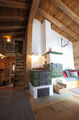 Kachelofen in hohem Wohnraum mit Holzdecke und Treppenaufgang