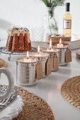 Alternativer Adventskranz. Vier Blechdosen mit Kerzen, im Hintergrund Eierlikörkuchen