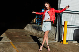 A brunette woman wearing a light t-shirt, a red leather jacket and a frayed denim skirt