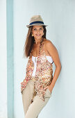 A brunette woman wearing a sequinned waistcoat, a white top, a light trousers and a hat