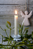 Christmas-tree candle on sprig of mistletoe in front of wooden angel