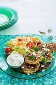 A green plate with zucchini, mint and feta grilled patties garnished with mint leaves and crumbled feta