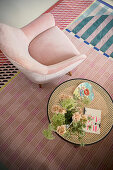 Rosafarbener Sessel und Beistelltisch auf bunt gemustertem Teppich