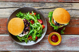 Burger mit Zwiebeln, Tomatensauce und Rucolasalat (Aufsicht)