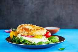 A bagel with a fried egg, lettuce and tomatoes