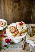 Festive vanilla and raspberry swiss roll with cream cheese filling and gold dust on wooden rustic surface