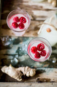 Festive gingerbeer in bottles and glasses served with raspberries on a rustic wooden surface with ice