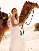 A young woman wearing a long white wedding dress with a camel