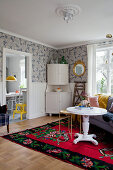 White corner cabinet against patterned wallpaper with round white table and sofa on rug in foreground