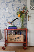 Vintage serving trolley against patterned wallpaper next to open double door painted white