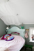 Bett mit Bettvorhang im Mädchenzimmer mit grauer Wand und Dachschräge