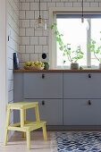 Graue Küchenzeile an gefliester Wand, im Vordergrund Trittleiter