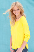 A young blonde woman wearing a yellow jumper against a blue background