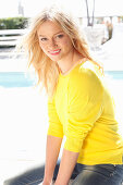 A young blonde woman outside wearing a yellow jumper and jeans