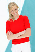 A young blonde woman wearing a red, short-sleeved jumper against a blue background