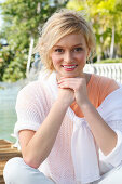 A young blonde woman wearing a white summer jumper by the sea