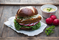 A lye bread roll with vegan meatloaf, coleslaw, radishes, lettuce and mustard