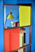 View of table lamp and collection of ceramics on sideboard seen through screen with coloured glass inserts