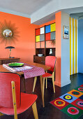 Dining area and sideboard in retro interior with orange wall