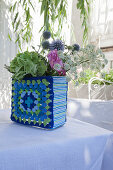 Blumen in einer Vase mit blau-grün gehäkelter Hülle