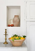 Fresh lemons in terracotta bowl below terracotta jug in niche