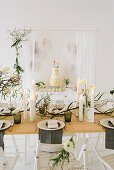 Gedeckter Hochzeitstisch mit Frühlingsblumen, trockenen Zweigen und Cylinderkerzen, im Hintergrund Buffet mit Hochzeitstorte