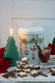 Glühwein, Zimtsterne, Weihnachtsstern, tannenbaumförmige Kerze und Blechdose