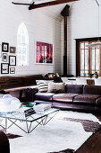 Glass coffee table and vintage leather couch in the living room with white wooden paneling and pointed arch windows in a former church