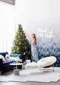 Blond woman decorates Christmas tree in corner of room with cozy seating