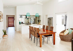Long dining table with wicker chairs, open kitchen with island in the background