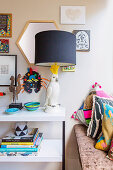 Console with table lamp, bowl and books next to bench with decorative pillows