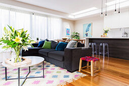 Round coffee table with bouquet and upholstered sofa, in the background a kitchen counter with bar stools in an open living room