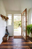 Wardrobe rail with hats and open entrance door in hallway with rustic floorboards