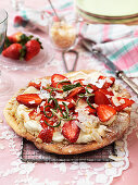 Sweet pizza with almond cream, whipped cream, strawberries and rosemary