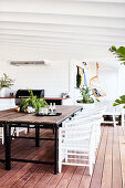 Dining table with rustic wooden top and white rattan chairs on veranda