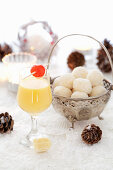 A glass of eggnog, and white egg liqueur chocolate truffles in a silver bowl