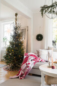 Red blanket on sofa next to Christmas tree in living room