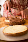 A cake being made: chocolate cream being spread onto a halved cake