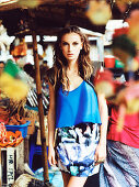 A brunette woman wearing a blue top and a batic skirt at a market