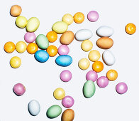 Colourful sugared almonds and chocolate beans on a white surface