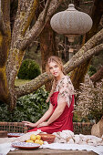 A young woman wearing a red dress sitting at a garden table