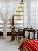 View across bed to wooden table in front of windows with louvre blinds