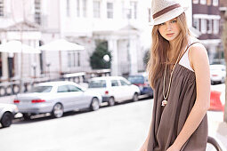 A young woman wearing a hat and a brown summer dress