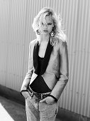A blonde woman wearing a blazer and jeans in front of a corrugated wall (black-and-white shot)