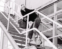 Blonde Frau in schwarzer Jacke, Jeans und High Heels auf Industrietreppe (s-w-Aufnahme)