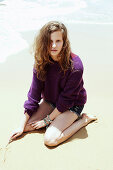 A young woman wearing a purple jumper and short on a beach