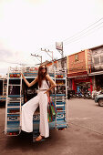 A young woman wearing a white jumpsuit standing on the back of mini van