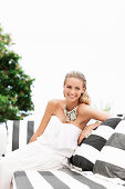 A blonde woman on a terrace wearing a white, off-the-shoulder dress