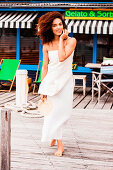 A dark-haired, barefoot woman wearing a white top and a white skirt